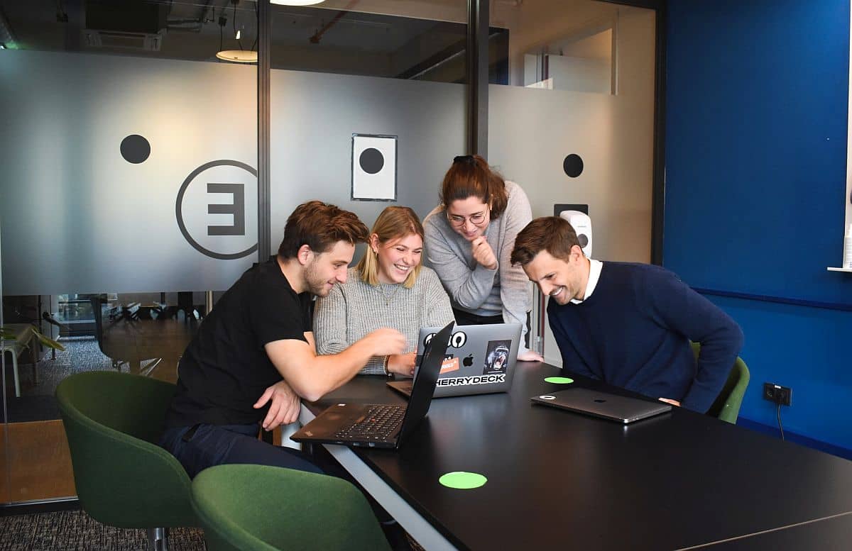 four young professionals huddle around a single laptop; Discovering Solutions for SaaS concept