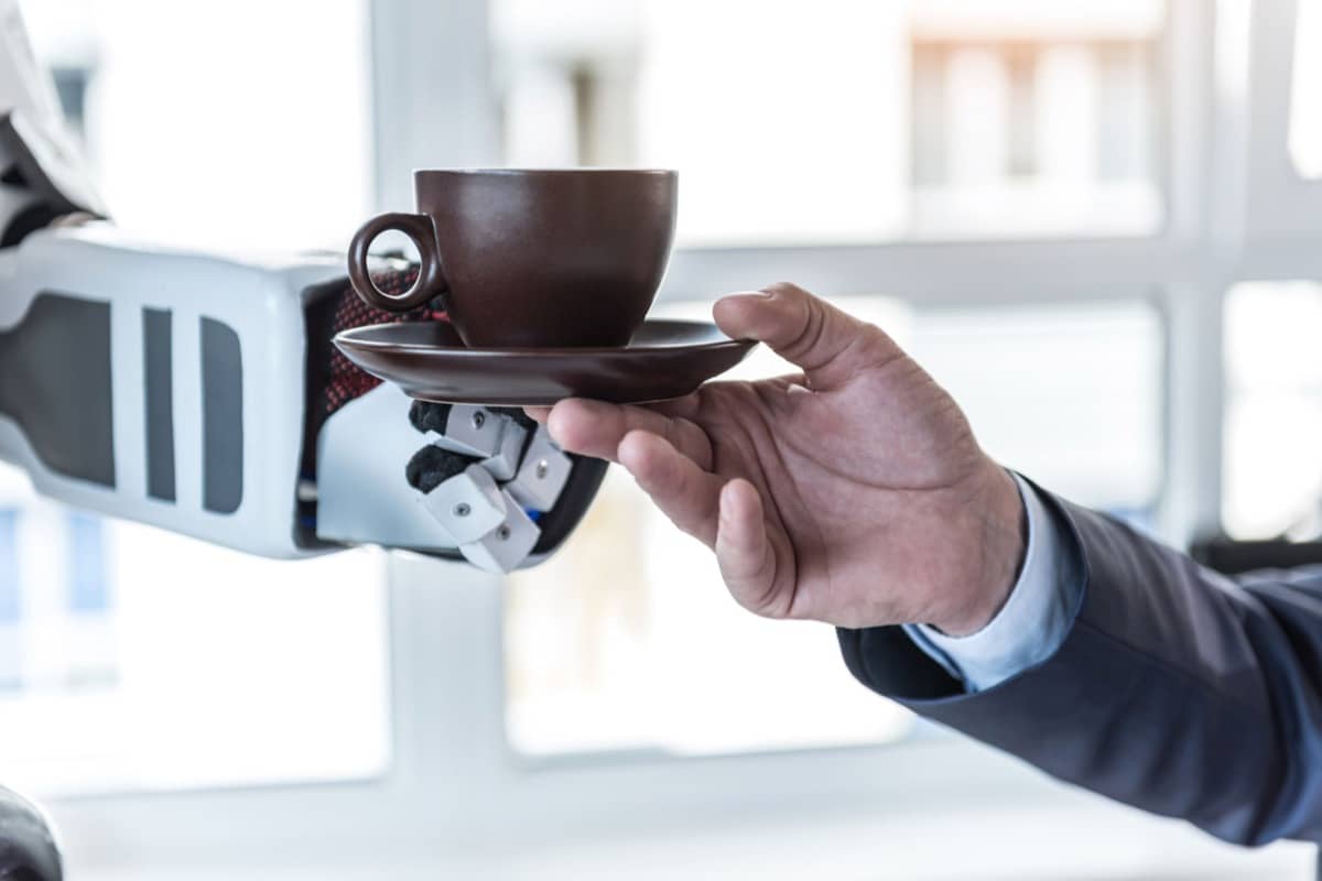 Close up male hand is taking cup of delicious espresso from robot in office; uncanny valley concept