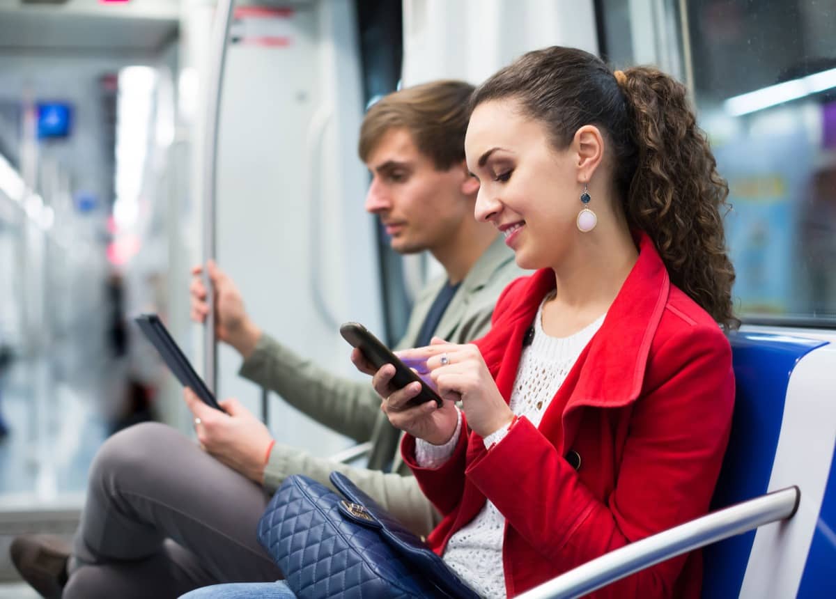 Happy couple reading smartphone and e-book in metro car; trust concept