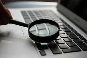 magnifying glass examining a laptop; Discovering Solutions for SaaS concept